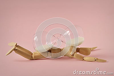 Wooden mannequin lying under hourglass on pink background - Concept of stopping time, health and aging Stock Photo