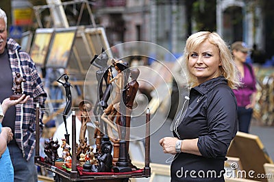 Wooden mini sculptures put up for sale during street fair, woman artist standing near to sell them Editorial Stock Photo