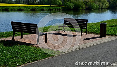 A wooden modern park bench with a metal embossed structure stands in a park by the river where cyclists stop for a snack on the ro Stock Photo