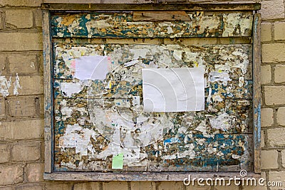 Wooden notice board on a white brick wall. Old painted wood with scraps of paper ads. Blank for paper advertisement. Mock up Stock Photo