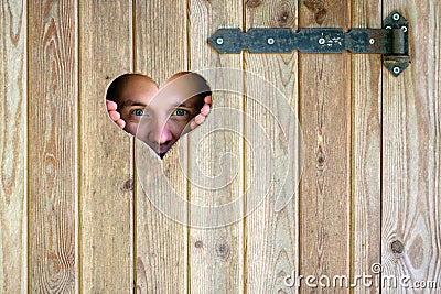 Wooden outdoor toilet with heart on the door. A man looks through a heart-shaped window. Stock Photo