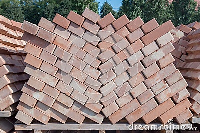Wooden pallet with red building bricks for transportation on backdrop of trees. They laid diagonally in two columns. Stock Photo