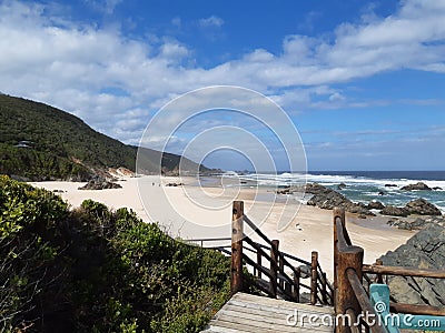 Wooden path leading to secluded beach with rocks and coastal bush Stock Photo