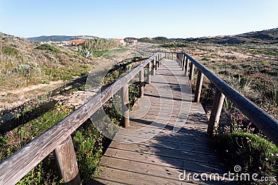 Wooden path from sunny beach to village through rural landscape, Portugal. Green hills in peaceful natural area Stock Photo