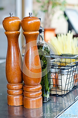 Wooden pepper mills, a bottle of extra virgin olive oil with spices and herbs, salt shakers on on a stainless surface Stock Photo