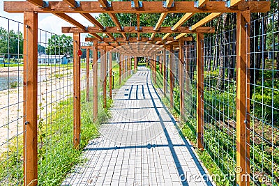 Wooden pergola (treillage) above cobblestone sidewalk leading along lake shoe and forest. Stock Photo