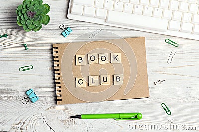 Wooden phrase Book club in workspace on paper notepad with computer keyboard, supplies and green plant on light wood background Stock Photo