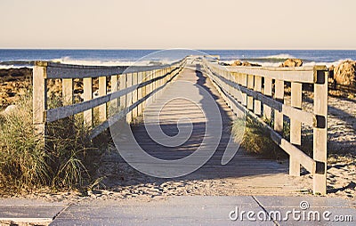 Wooden pier with grass on Atlantic ocean coast, Portugal. Wooden boardwalk to sea on rocks shore. Empty walkway in dunes at dawn. Stock Photo