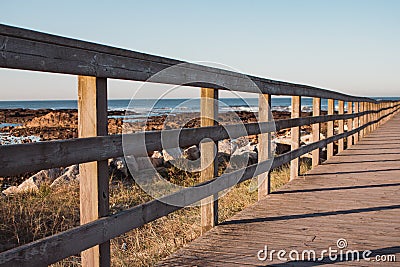 Wooden pier with grass on Atlantic ocean coast, Portugal. Wooden boardwalk to sea on rocks shore. Empty walkway in dunes at dawn. Stock Photo