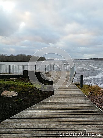 Wooden pier that leads to a viewing platform. Wooden site in front of the river. Wooden walkboard with a fence. Stock Photo