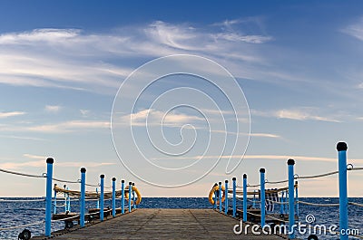 Wooden platform with blue posts with ropes and orange lifebuoys on the background of the sea and sky with clouds Egypt Dahab South Stock Photo