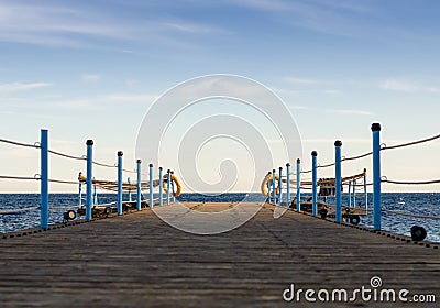 Wooden platform with blue posts with ropes and orange lifebuoys on the background of the sea and sky with clouds Egypt Dahab South Stock Photo