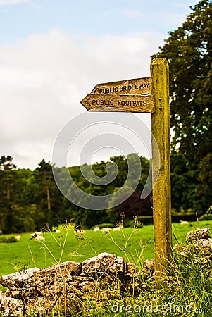 Wooden public footpath sign in field next to a wall Stock Photo