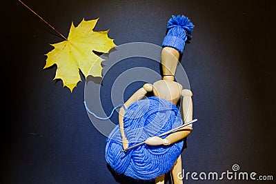 Wooden puppet doll holds a ball of blue yarn and crochet hook in its hands, and wears a knitted winter hat Stock Photo