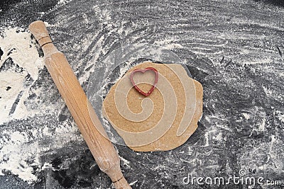 Wooden rolling pin and dough with heart-shaped print. Baking with love. Biscuit making process Stock Photo