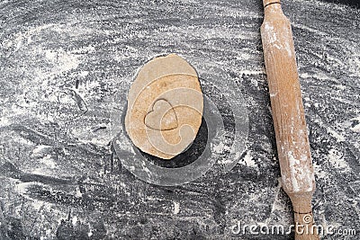 Wooden rolling pin and piece of dough with heart-shaped print. Baking with love. Biscuit making process Stock Photo