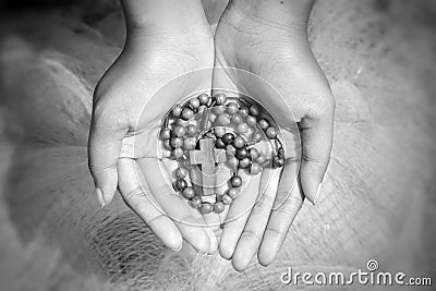 Wooden rosary beads in an young woman open hands with Jesus Christ holy cross crucifix on black and white abstract art background. Stock Photo