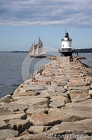 Sailboat Passes by Lighthouse on Edge of Breakwater in Maine Editorial Stock Photo