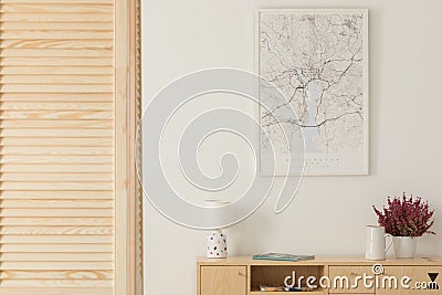 Wooden screen next to wooden cabinet with lamp, vase and heather in white pot, map in white frame on the wall Stock Photo