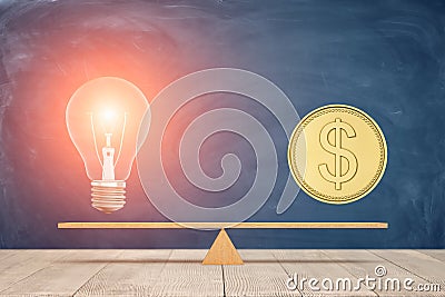 A wooden seesaw keeping the balance with a large golden coin and a glowing lamp standing on each side. Stock Photo