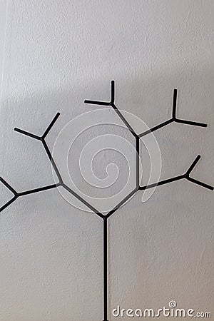 On a wooden shelf, against a background of white wallpaper, stands a figure of a tree made of steel wire. Stock Photo