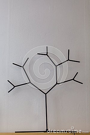 On a wooden shelf, against a background of white wallpaper, stands a figure of a tree made of steel wire. Stock Photo