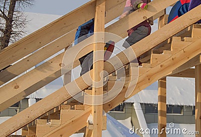 Wooden slide for children in winter, children with sledges and tubing climb the hill, fun at Christmas Stock Photo