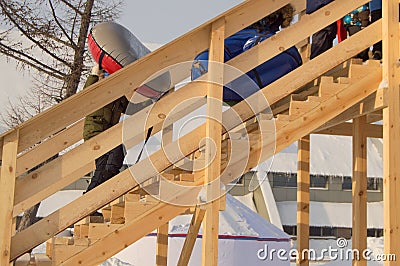 Wooden slide for children in winter, children with sledges and tubing climb the hill, fun at Christmas Stock Photo