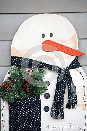 A wooden snowman winter decoration with a cloth scarf and pocket filled with winter greens, pinecones and berries Stock Photo