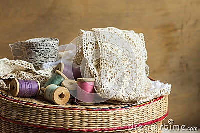 Wooden spools of multi color threads, rolls of beige and grey cotton lace on sewing rattan wicker basket, hobby, crafts Stock Photo