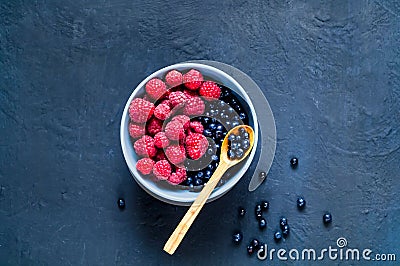 Wooden spoon with bilberry and raspberries in blue bowl, the concept of organic berries on dark background. Berry picking Stock Photo