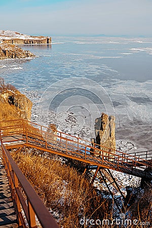 Wooden staircase with metal railings, very steep at great height, leading down to the sea, covered in ice and snow Stock Photo
