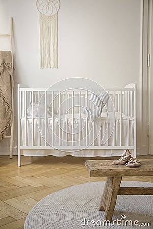 Wooden stool with shoes on round rug in bright baby`s bedroom interior with white cradle Stock Photo