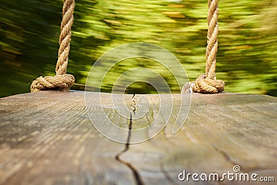 wooden swing with thick ropes. the camera is standing on a swing, blurred background is a park, a wooden swing Stock Photo