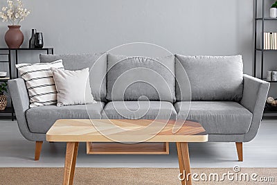 Wooden table and big grey couch with pillows in living room of trendy apartment, real photo Stock Photo