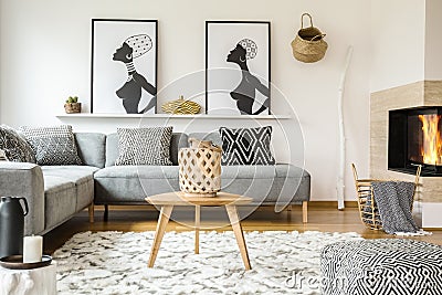 Wooden table on carpet in african living room interior with patterned cushions on grey sofa. Real photo Stock Photo