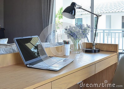 Wooden table with computer notebook,pencil,lamp and artificial flowers in modern working area at home Stock Photo