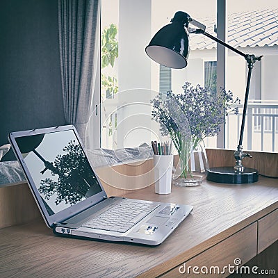 Wooden table with computer notebook,pencil,lamp and flowers in working area Stock Photo