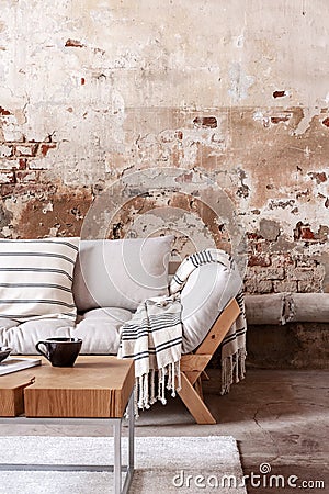 Wooden table in front of grey couch with blanket in wabi sabi living room interior with red brick wall Stock Photo