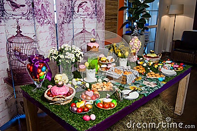 A wooden table with a grassy tablecloth and Easter treats: eggs, cakes, chocolate eggs, meringues Stock Photo