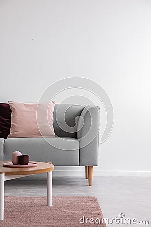 Wooden table on pink carpet in front of grey settee with pillows in white flat interior. Real photo Stock Photo