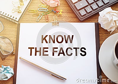 On a wooden table there is an office sheet of paper with the text KNOW THE FACTS. Business workspace with calculator, glasses, pen Stock Photo