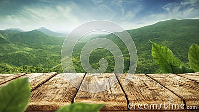 Wooden table top with green mountain background. Blue sky with sun light and green small leaves. Stock Photo