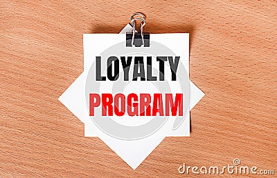 On a wooden table under a black paper clip lies a sheet of white paper with the text LOYALTY PROGRAM Stock Photo