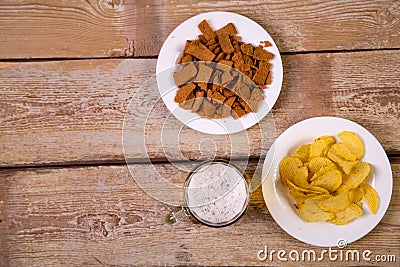 On a wooden table are white plates with crispy croutons and potato chips. Stock Photo