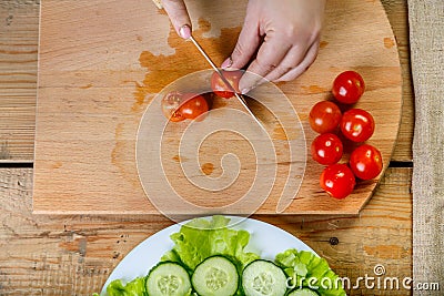 On a wooden table, a woman knives a regimen of tomatoes Stock Photo