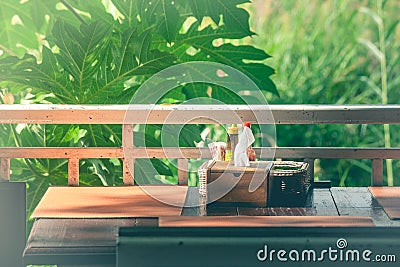 Wooden tissue box and garnish in basket salt, pepper, toothpick, sauce on table with green trees and sunlight background. Stock Photo