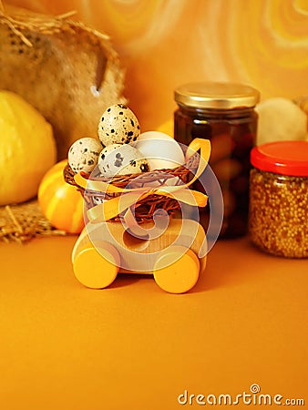 Wooden toy car with a basket of quail eggs on a bright yellow background painted in pastels, pumpkins Stock Photo