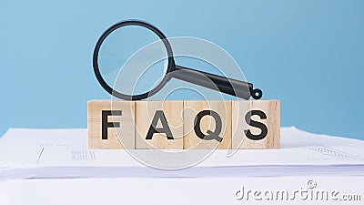 wooden toy cubes with text FAQS on a blue background with magnifying glass Stock Photo