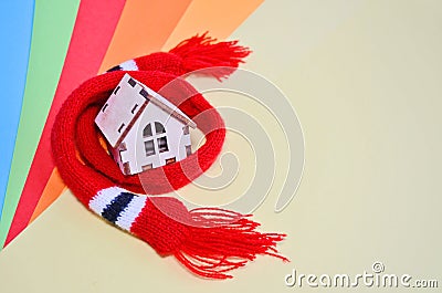 Wooden toy house in a red scarf on a rainbow colored background, warm house, insulation of house, copyspace Stock Photo